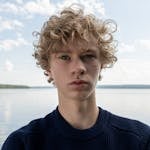 Close-up portrait of a blond teenager with curly hair at a lake, daytime.