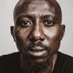 Intense close-up portrait of an African man with a serious expression and facial hair.